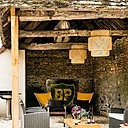 Le salon d’extérieur est chapeauté par une toiture ancienne dans son jus. Accrochés sur la poutraison, des luminaires en osier tressé apportent une touche contemporaine et cosy.