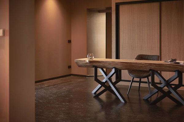 A l’accueil du restaurant, une table en bois brut retravaillé façon demi tronc monté sur un piètement géométrique et sculptural en croisillons, création Exsud.