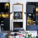 De part et d’autre de la cheminée du salon, des bibliothèques dessinées par l’agence Ronjat et Poggioli intérieurs, qui offrent des niches colorées et éclairées pour mettre en valeur une collection d’art primitif. Appliques, « Formes noires » avec réflecteur moule,  création Serge Mouille. Canapés, Minotti. Tables basses avec plateau en marbre et acier Cortex dessinées par l’agence Ronjat et Poggioli intérieurs. Se reflétant dans le miroir, un fusain de Robert Longo.