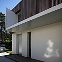 A gauche, un oriel moderne en métal laqué blanc protège l’entrée, de l’intrusion de la pluie, fait entrer la lumière à l’intérieur et permet d’accéder à la cuisine. A droite, les percements verticaux suivent le mouvement dynamique de l’escalier intérieur. La parure en bois dissimule les descentes d’eau pluviale.