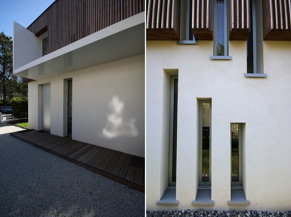 A gauche, un oriel moderne en métal laqué blanc protège l’entrée, de l’intrusion de la pluie, fait entrer la lumière à l’intérieur et permet d’accéder à la cuisine. A droite, les percements verticaux suivent le mouvement dynamique de l’escalier intérieur. La parure en bois dissimule les descentes d’eau pluviale.