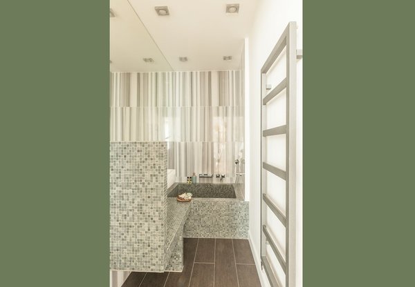 Dans un camaïeu de gris très élégant, la salle de bains, dédiée aux amis et invités, est revêtue d’un carrelage mural en marbre Striato, strié verticalement. Le miroir agrandit la pièce. La douche bain pataugeoire est recouverte de petits carreaux de mosaïque en pâte de verre. Au sol, les dalles en grès cérame agrandissent l’espace. Devant, un muret cache le coin toilettes intégré.