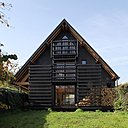 Lignes pures et minimalistes, toit imposant en tôle ondulée noire très couvrante pour cette maison. La maison, en bois, est enduite de goudron de pin noir.