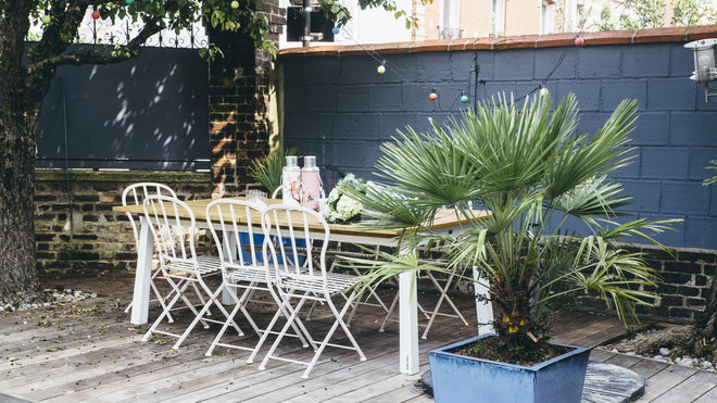 Dans le jardin, les murs en brique ont été repeints en bleu et une grande table permet de prendre les repas dehors lorsque les beaux jours arrivent.