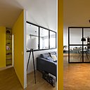 Dans l’entrée, une niche étroite a été pratiquée pour offrir une colonne de rangement. Lampadaire Tripod, AM.PM. La verrière façon atelier peinte en noir contraste sur les murs de couleur jaune (peinture satinée, CH1 0593 Jaune Reynolds, Cromatic). Une tablette murale vide-poches avec rebord, en bois, anime le mur de l’entrée.