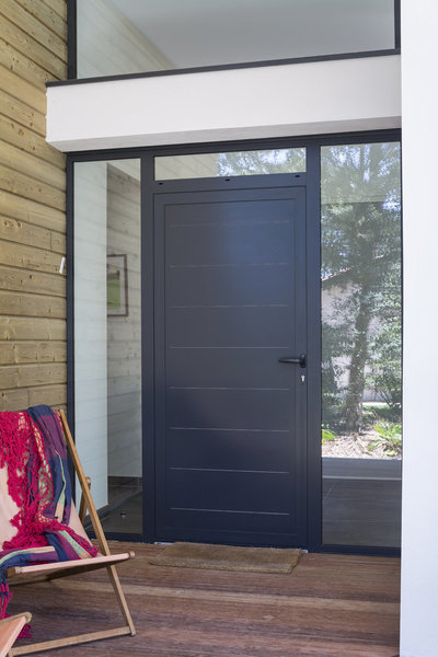 Pour créer une entrée accueillante, l’architecte a conçu un ensemble composé de châssis fixes et d’une porte d’entrée en aluminium 1 vantail.
