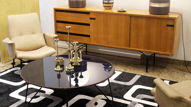 Dans la Galerie Toulousaine, table basse des années 1950 avec piètement tubulaire coudé. Enfilade de Gérard Guermonprez en chêne clair avec 2 portes coulissantes et tiroirs sur piètement en métal laqué noir, années 1950.