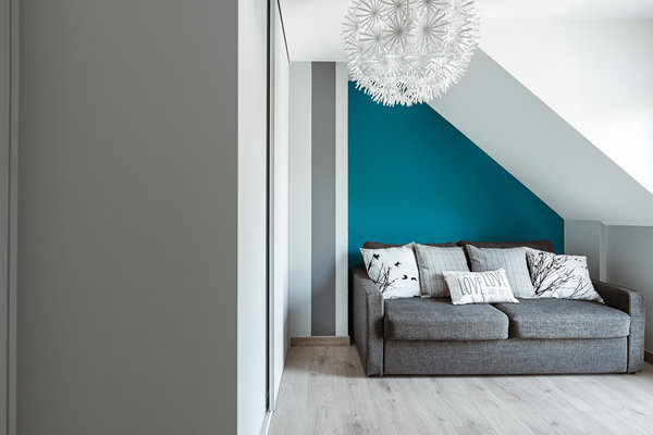 La chambre d’ami avec soupente mis en valeur par un mur coloré contrastant avec un canapé gris.