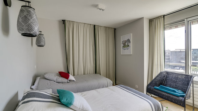 La chambre d’amis, dotée de deux fenêtres dont l’une occultée par des rideaux. Appliques lumineuses, La Redoute Intérieurs.