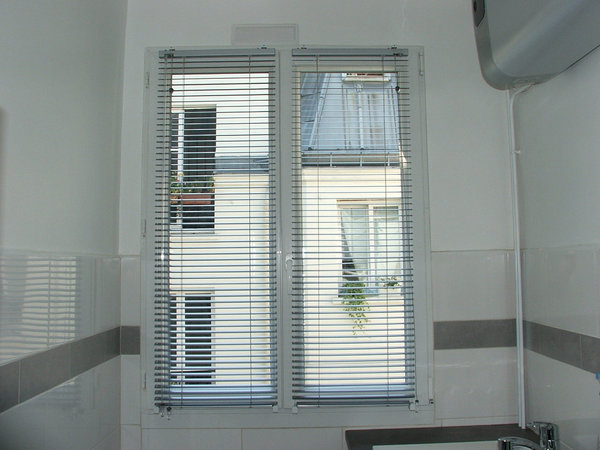 Après la pose : constitué d’une succession de lamelles horizontales en aluminium, le store vénitien transforme la baie vitrée en un large écran de diffusion lumineux.