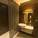 Les murs de la salle de bains, avec douche à l’italienne et rideau perlé, sont recouverts de carreaux de grès cérame qui imitent l’écorce d’un arbre.