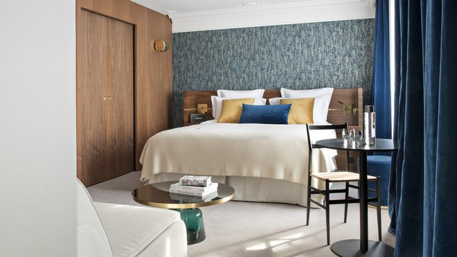 Dans la chambre, la tête de lit en noyer, dessinée sur mesure, est personnalisée par un listel en laiton qui fait écho à la matière des appliques. Les teintes des papiers-peints graphiques s’accordent avec celle des rideaux en velours pour composer un espace cosy.