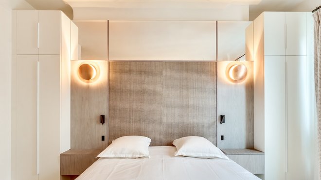 Dans la chambre des propriétaires, le mur qui accueille la tête du lit a été habillé d’un panneau en bois dessinant un effet de peau de crocodile (Oberflex) et encadré de deux placards symétriques. Appliques lumineuses, modèle Lederam W, chez Castellani and Smith.