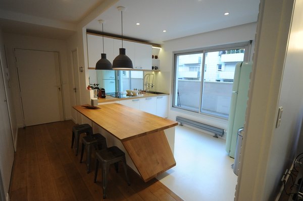 Après les travaux : un plan de travail et un comptoir en chêne avec un angle biseauté pour dégager de la place pour les jambes en position assise. Réfrigérateur d’esprit années 1950, de couleur pastel, Smeg. Suspensions, Muuto. Tabourets de chez Tolix.