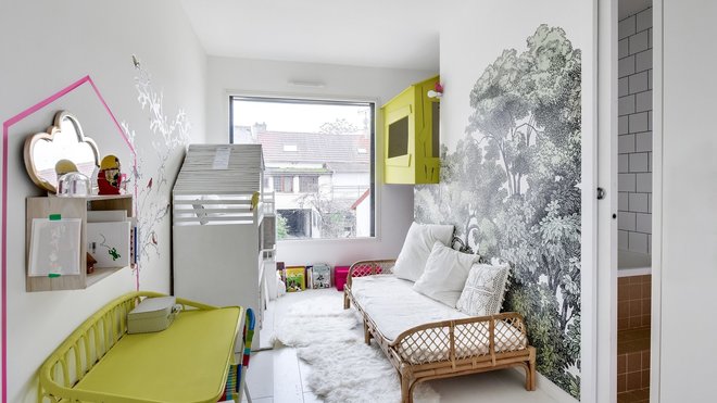 La chambre de l’une des deux filles avec mur de papier-peint, modèle BelleWood chez Rebel Walls. La cabane peinte en vert anis permet de communiquer avec l’autre chambre d’enfant.
