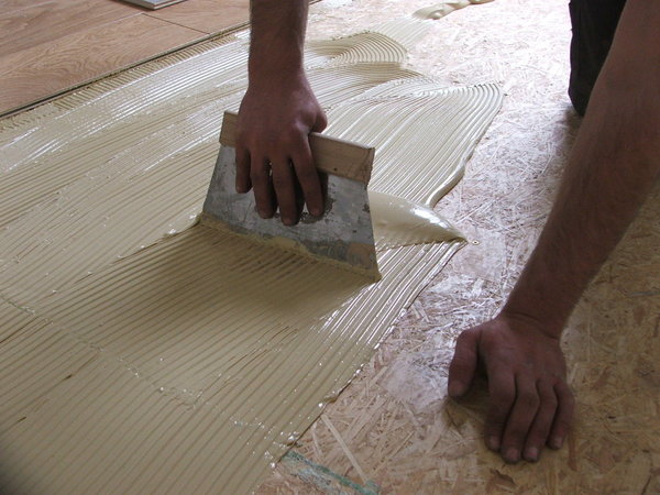 Etape 19 : La colle est étalée avec la spatule colle parquet. Il est primordial de bien progresser par zones de demi-mètre carré et cela dans le but d’avoir un temps ouvert d’encollage suffisant, au risque de voir le dépôt de colle sécher et durcir.