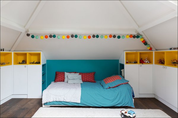 Sous la charpente, une chambre d’enfants encadrée par de nombreux rangements et des teintes qui font référence au domaine des jouets.