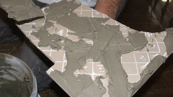 Etape 13 : à noter qu’on réalise un double encollage, la colle est appliquée sur la surface à carreler et sous les carreaux de ciment.