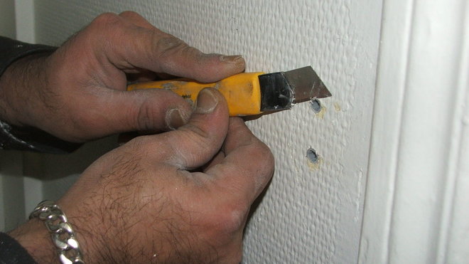 Etape 2 : Avant de travailler le revêtement de toile de verre, on enlève toutes les irrégularités comme les chevilles ici qu’on retire à l’aide d’un cutter.