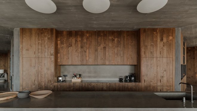Sur les portes des rangements, le veinage des lames de bois est mis en valeur. La table de l’îlot de cuisine, avec son plateau recouvert d’un enduit de béton, dialogue avec l’architecture intérieure.