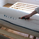 Etape 6 : après avoir enlevé la toile de jute qui protège le matelas, positionnez-le sur le lit dans le sens de la largeur avec la broderie Kipli au niveau des pieds. Découpez la protection en prenant soin de ne pas abîmer la housse.